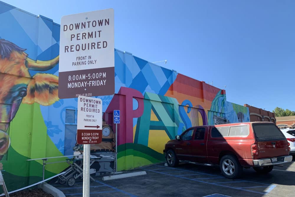 photo of a sign that says Downtown Parking Permit required, in front of a parking lot and colorfully painted building